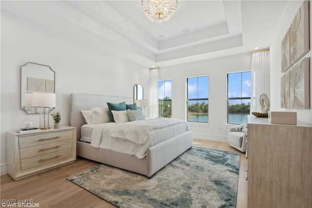 bedroom featuring a notable chandelier, a water view, light wood-type flooring, and a tray ceiling