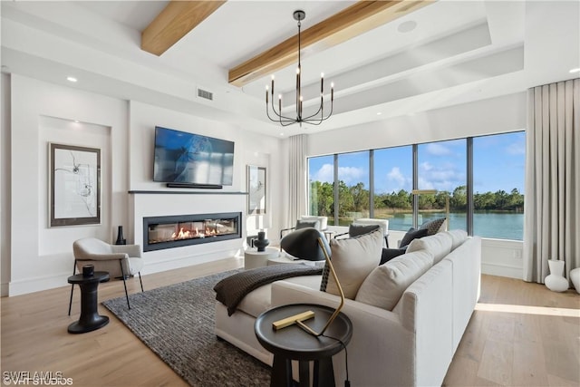 living room with beam ceiling, a raised ceiling, a chandelier, and light hardwood / wood-style floors