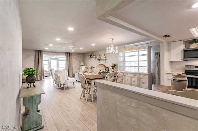 kitchen featuring stainless steel appliances, decorative light fixtures, white cabinets, ceiling fan with notable chandelier, and light wood-type flooring