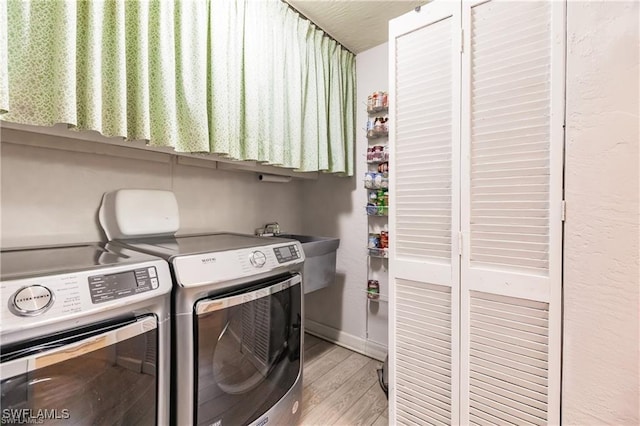 clothes washing area featuring washing machine and dryer, light hardwood / wood-style flooring, and sink