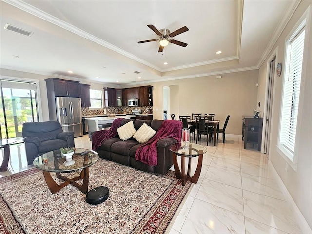 living room with a tray ceiling, ceiling fan, and crown molding