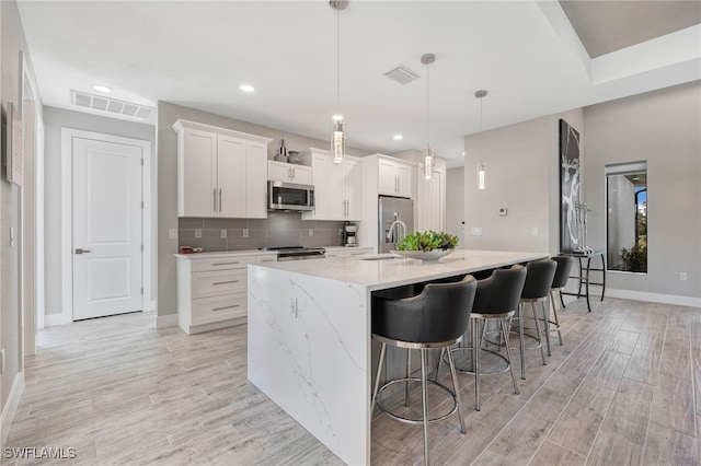 kitchen featuring pendant lighting, a kitchen breakfast bar, an island with sink, appliances with stainless steel finishes, and white cabinetry