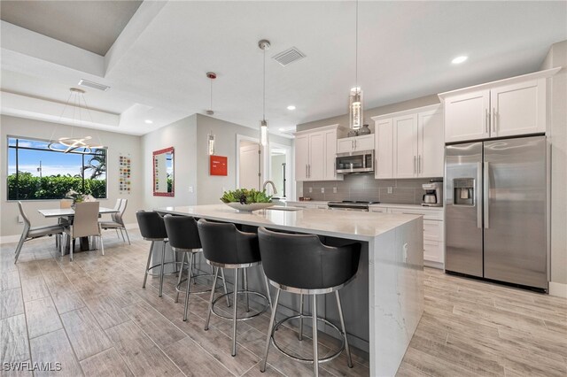 kitchen with white cabinets, decorative light fixtures, stainless steel appliances, and an island with sink