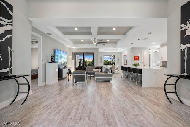 living room featuring ceiling fan, beamed ceiling, coffered ceiling, and light wood-type flooring