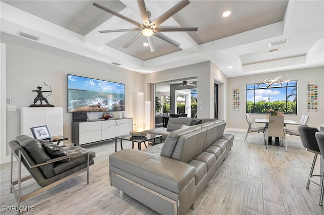 living room with a raised ceiling, coffered ceiling, and ceiling fan with notable chandelier