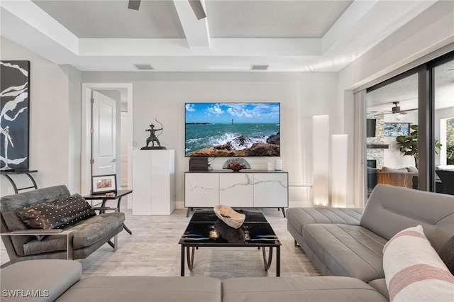 living room with beam ceiling, a raised ceiling, ceiling fan, and light hardwood / wood-style flooring