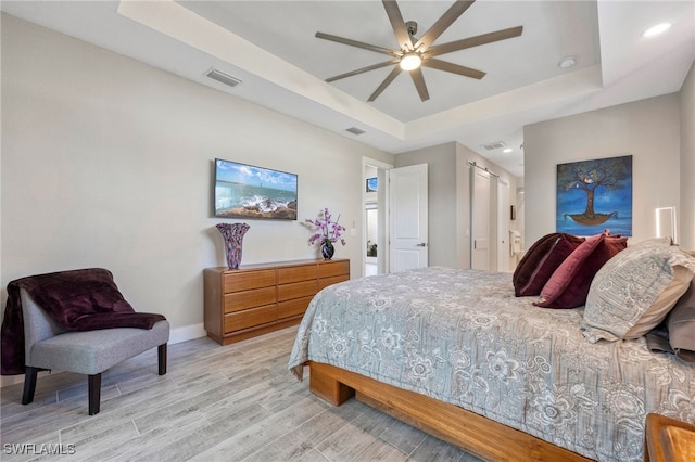 bedroom featuring a raised ceiling, ceiling fan, and light hardwood / wood-style flooring