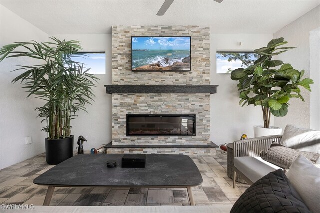 living room featuring a stone fireplace, ceiling fan, and a textured ceiling