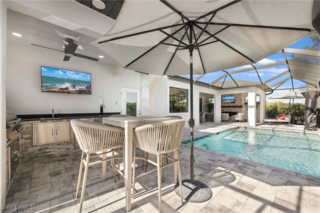 view of swimming pool featuring a lanai, ceiling fan, sink, exterior kitchen, and a patio