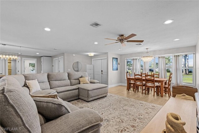 living room with light hardwood / wood-style floors and ceiling fan with notable chandelier