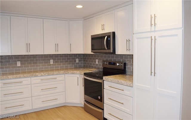 kitchen featuring light stone countertops, decorative backsplash, white cabinets, and stainless steel appliances