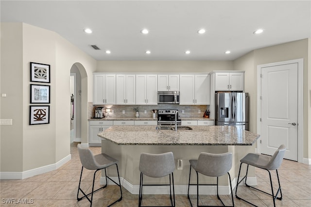 kitchen featuring white cabinets, stainless steel appliances, a kitchen island with sink, and a breakfast bar area