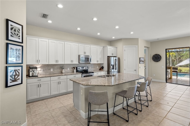 kitchen with a kitchen bar, light stone countertops, stainless steel appliances, a kitchen island with sink, and white cabinets