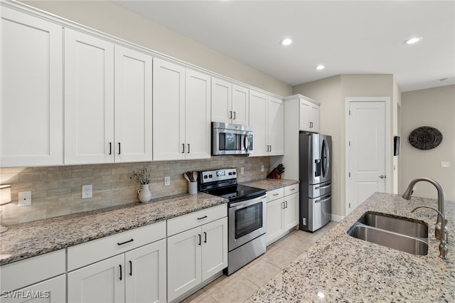 kitchen with appliances with stainless steel finishes, backsplash, light stone counters, sink, and white cabinetry