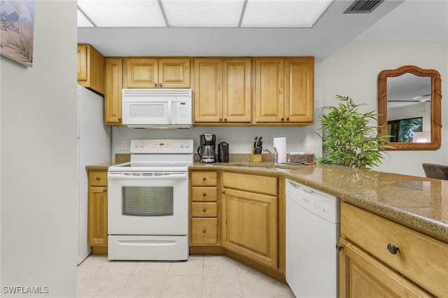 kitchen featuring light tile patterned flooring, white appliances, light stone counters, and sink