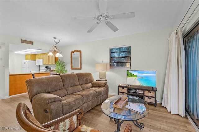 living room with ceiling fan with notable chandelier and light hardwood / wood-style flooring