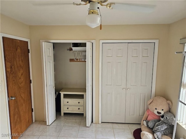 unfurnished bedroom featuring ceiling fan, light tile patterned floors, and multiple closets