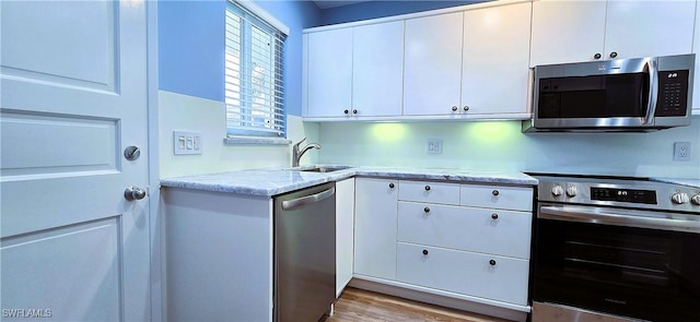 kitchen with stainless steel appliances, white cabinetry, sink, and light wood-type flooring