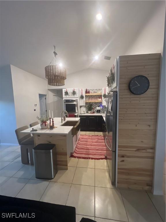 kitchen with double oven, refrigerator, an island with sink, lofted ceiling, and light tile patterned floors