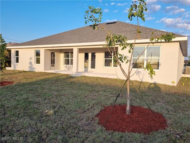 back of house with a shingled roof, a patio, a lawn, and stucco siding