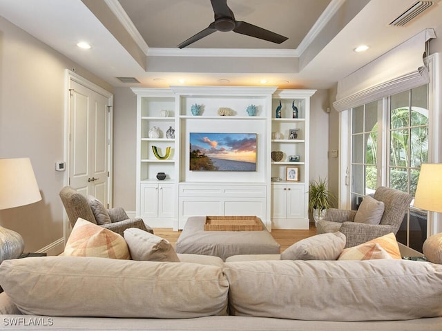 living room featuring crown molding, light hardwood / wood-style flooring, ceiling fan, and a tray ceiling