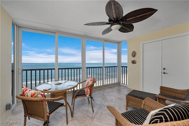 sunroom / solarium with ceiling fan, a water view, a healthy amount of sunlight, and a view of the beach