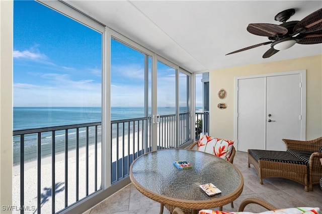 sunroom featuring ceiling fan, a water view, and a view of the beach