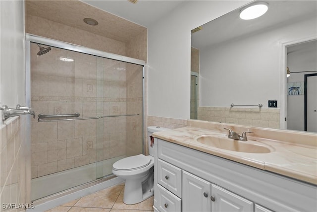 bathroom featuring tile patterned flooring, toilet, vanity, a shower with shower door, and tile walls