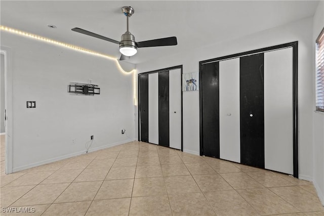 unfurnished bedroom featuring ceiling fan, light tile patterned flooring, and two closets