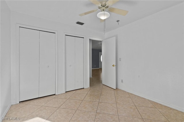 unfurnished bedroom with ceiling fan, light tile patterned floors, and two closets