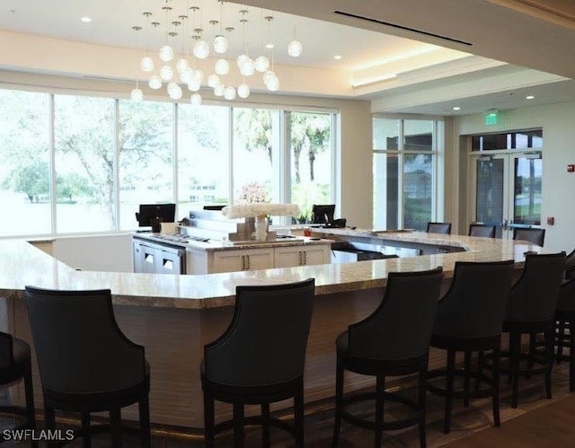 bar featuring white cabinetry, light stone countertops, a raised ceiling, and hanging light fixtures