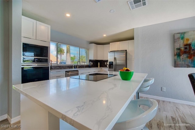 kitchen featuring white cabinets, light stone counters, a kitchen island, and appliances with stainless steel finishes