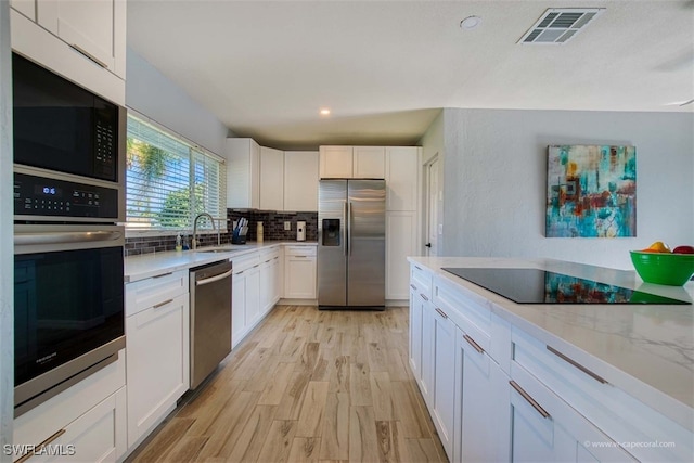 kitchen featuring light stone countertops, appliances with stainless steel finishes, tasteful backsplash, sink, and white cabinetry