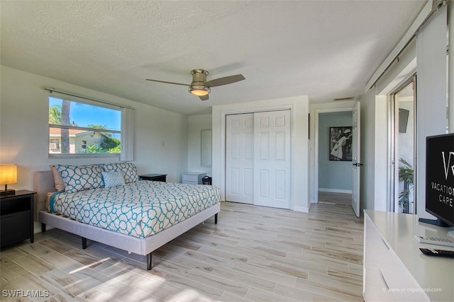 bedroom with ceiling fan, light hardwood / wood-style floors, a textured ceiling, and a closet