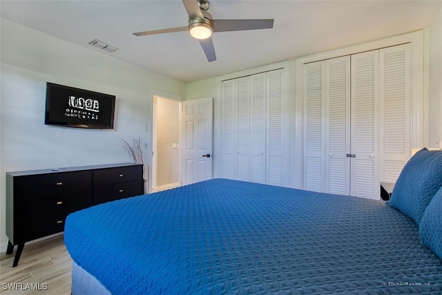 bedroom featuring light hardwood / wood-style flooring, ceiling fan, and multiple closets