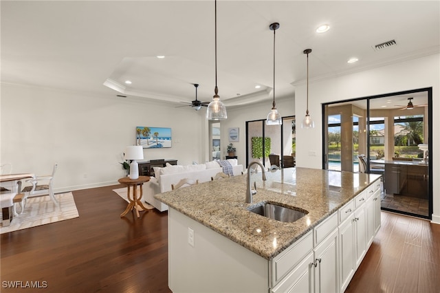 kitchen featuring sink, decorative light fixtures, an island with sink, light stone countertops, and white cabinets