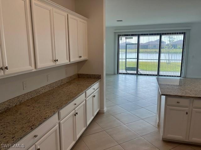 kitchen featuring white cabinetry, a water view, light stone counters, and light tile patterned floors