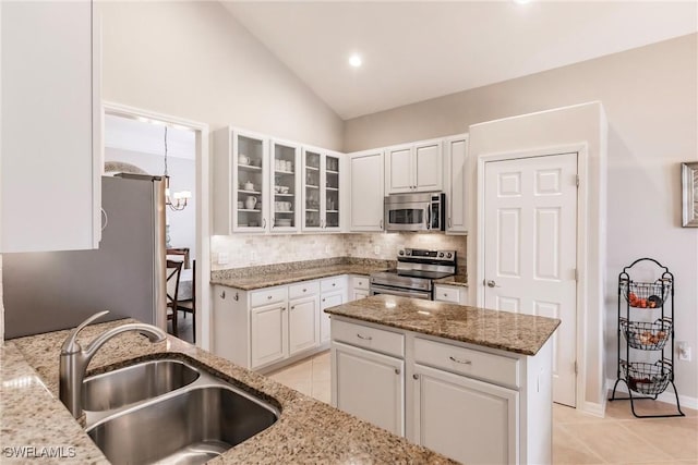 kitchen with sink, stainless steel appliances, a kitchen island, light stone counters, and white cabinets