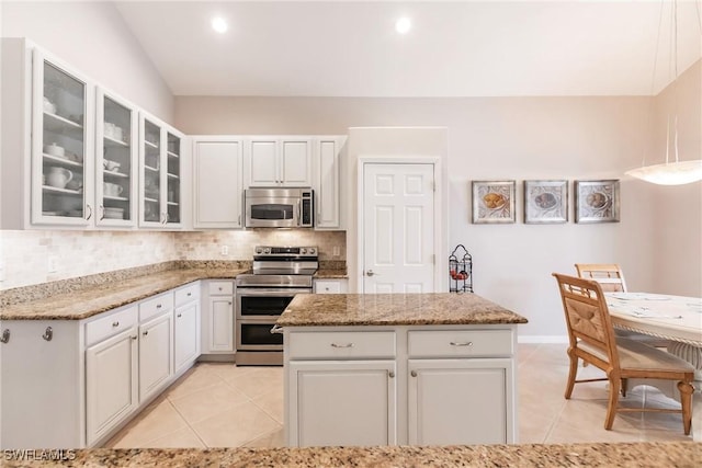 kitchen featuring decorative backsplash, appliances with stainless steel finishes, light stone counters, white cabinets, and a center island