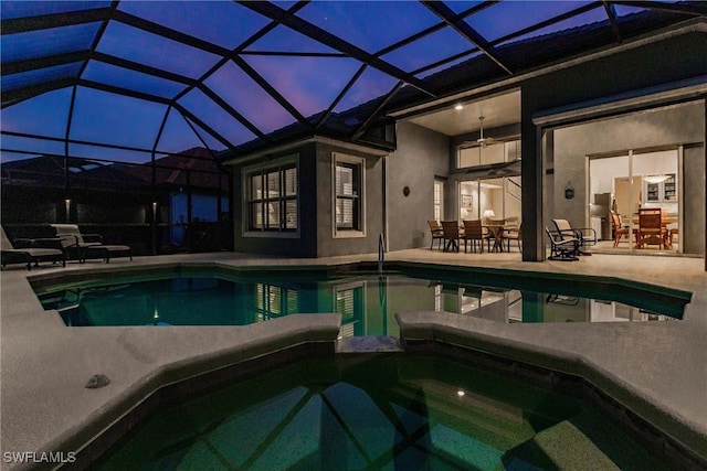 pool at dusk featuring ceiling fan, a lanai, a patio, and an in ground hot tub