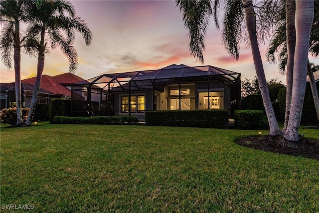 back house at dusk featuring a lawn and glass enclosure