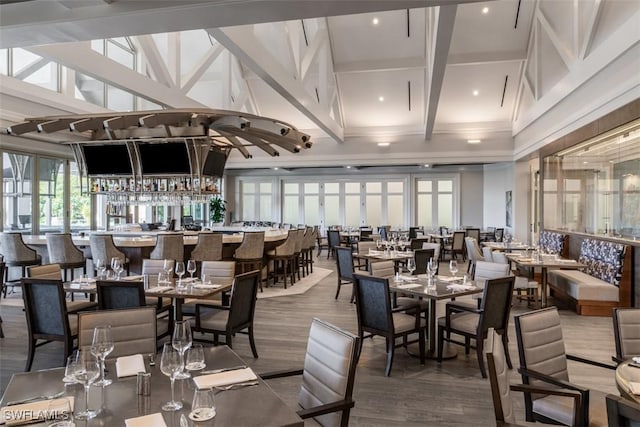 dining space with beam ceiling, hardwood / wood-style floors, and a high ceiling