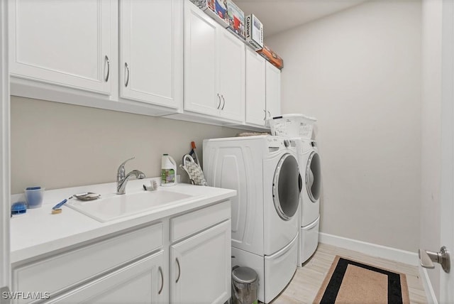 clothes washing area with washing machine and clothes dryer, sink, and cabinets