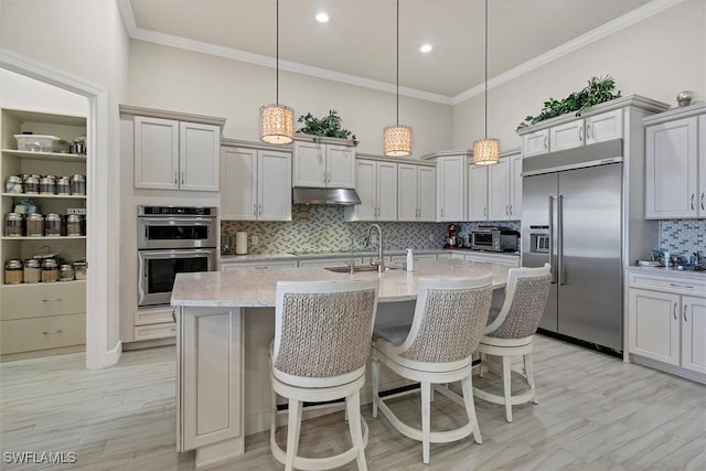 kitchen with light stone countertops, a kitchen island with sink, pendant lighting, and appliances with stainless steel finishes