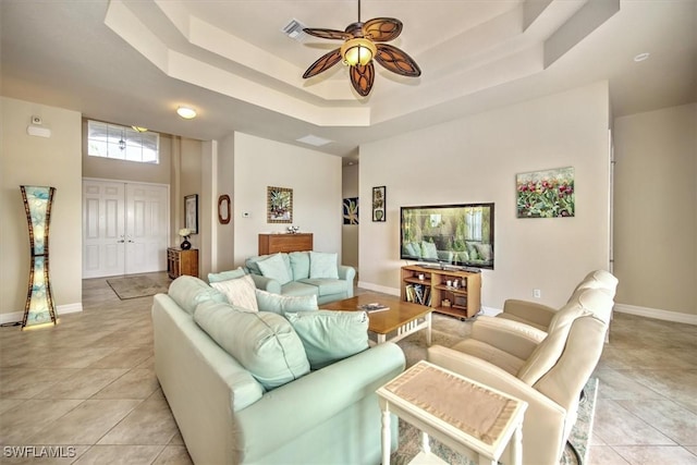 living room with ceiling fan, a raised ceiling, light tile patterned floors, and a high ceiling