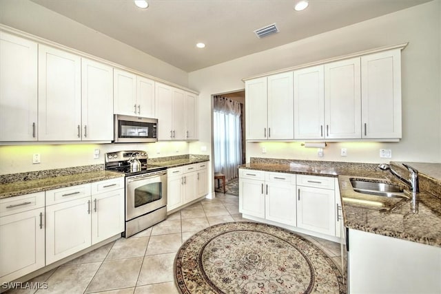 kitchen with stainless steel appliances, white cabinetry, dark stone counters, and sink