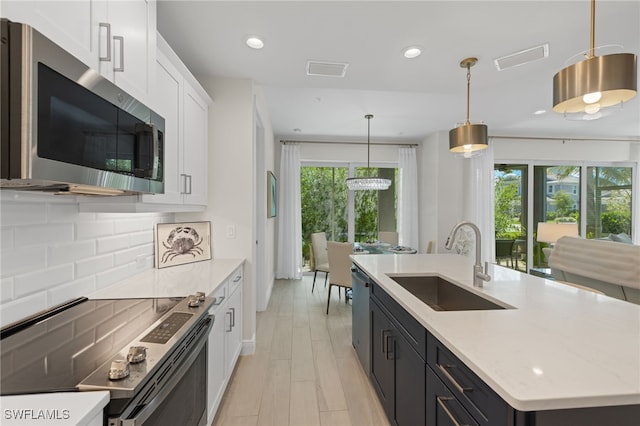 kitchen with white cabinets, stainless steel appliances, a sink, and decorative light fixtures