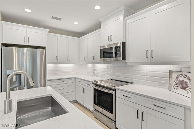 kitchen with stainless steel appliances, visible vents, decorative backsplash, white cabinetry, and a sink