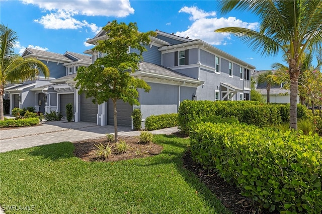 view of front of home featuring a garage, decorative driveway, a front yard, and stucco siding