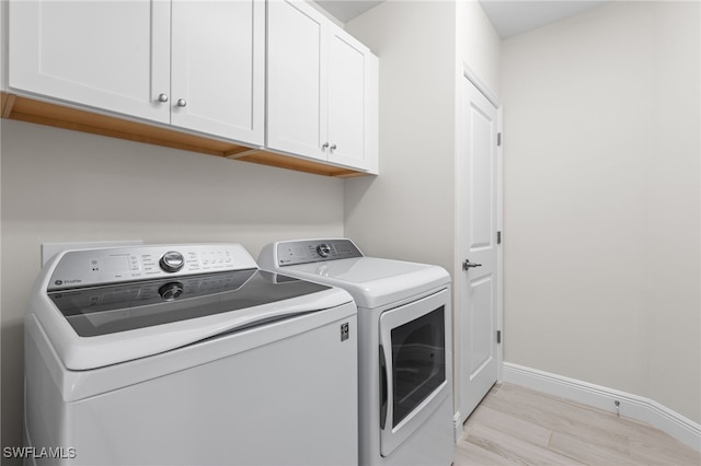 clothes washing area with separate washer and dryer, light wood-style floors, cabinet space, and baseboards